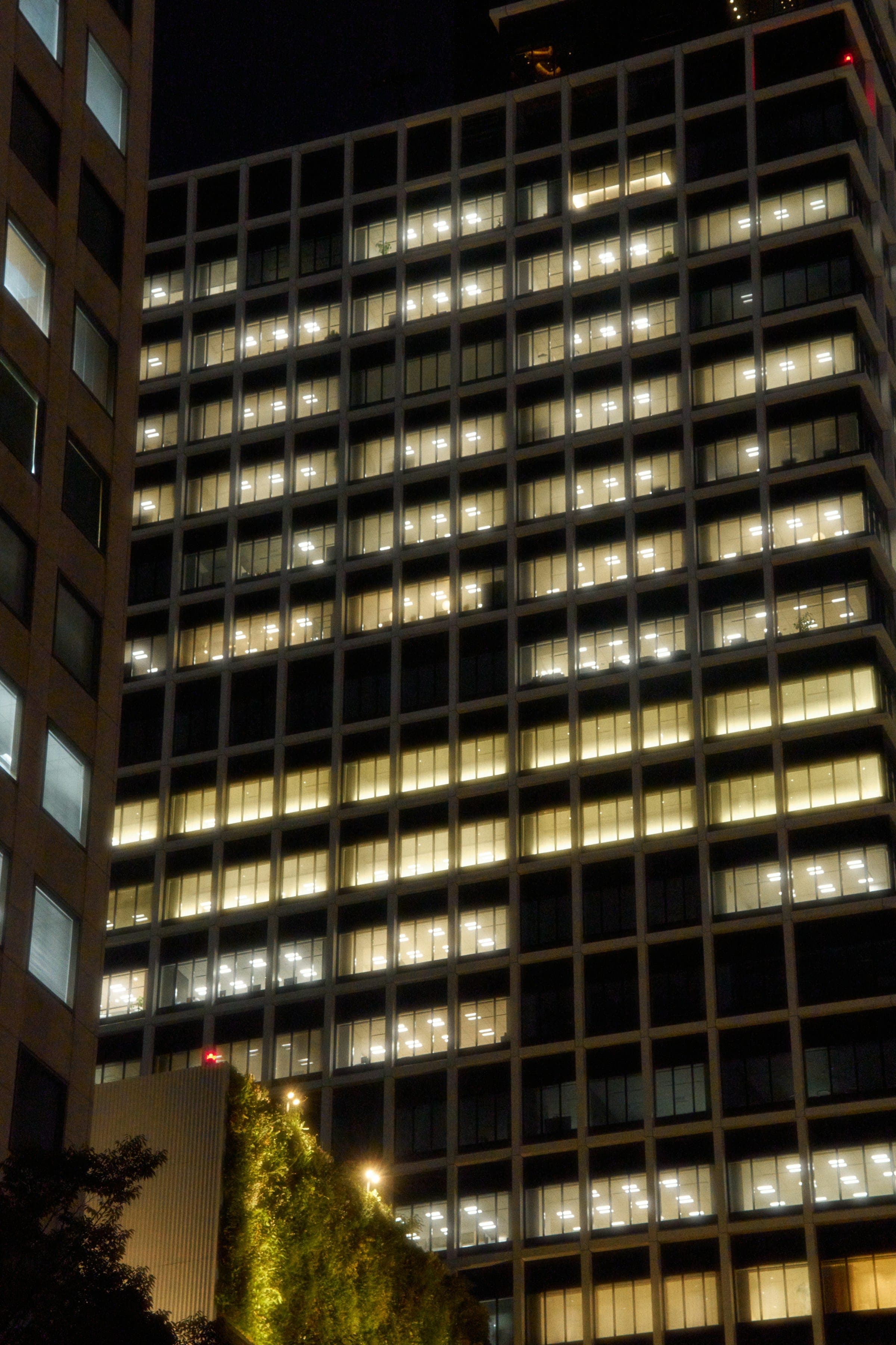 An office tower at night, its windows lit warm against the dark.