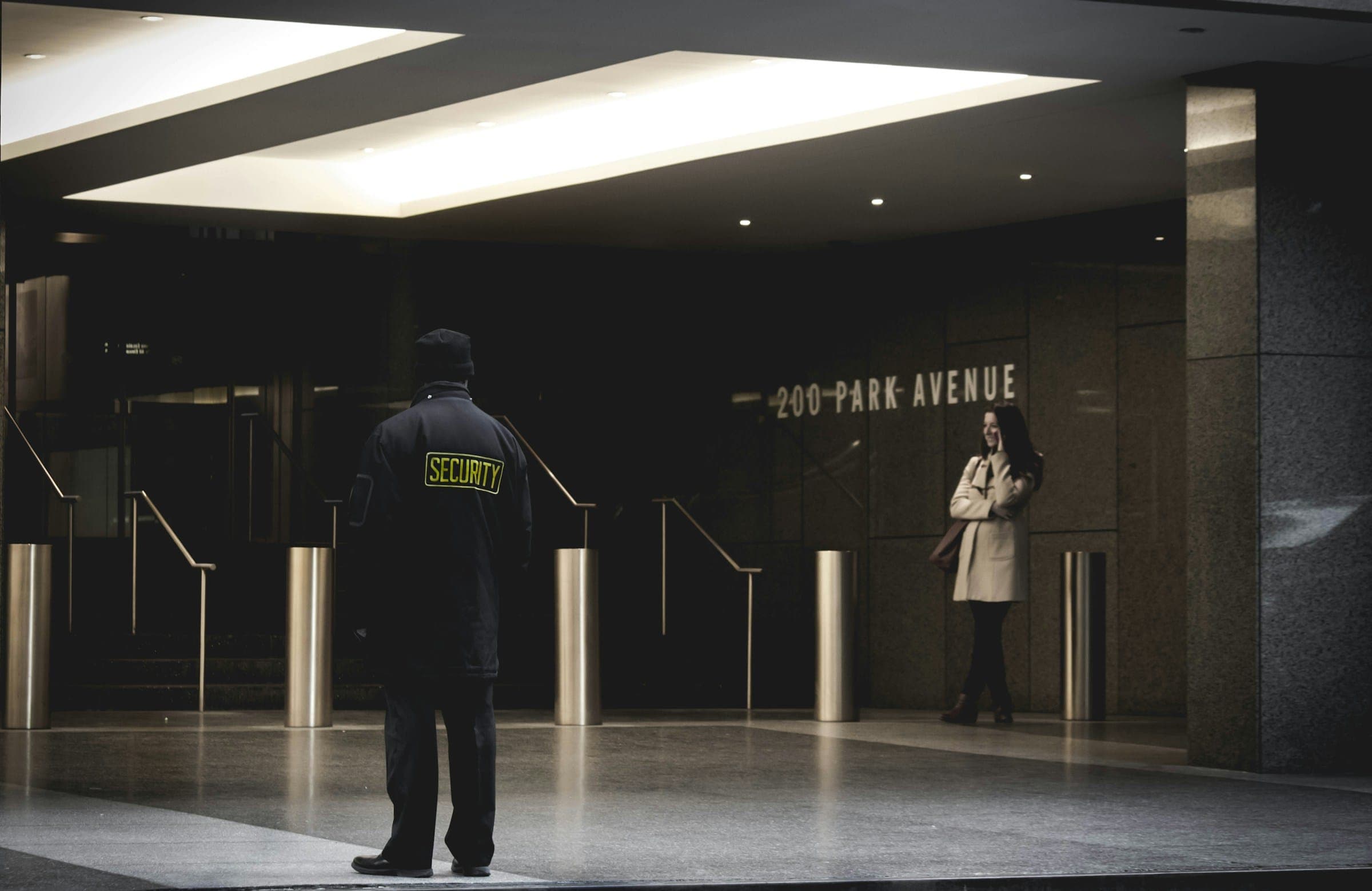 A security officer standing in a marble lobby at night, facing the entrance.